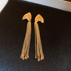 Detail of gold-plated fish tail earrings with long tassel chains on black background.