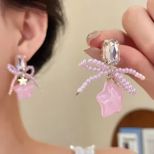 Close-up of pink beaded bow earrings featuring a resin star and crystal stud detail.