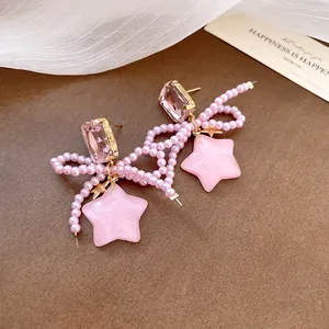 Detailed close-up of pink pearl bow earrings with resin star charms and pink gems