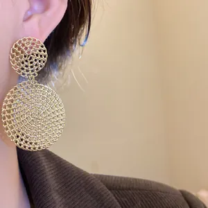Macro view of elegant golden hollow circular woven drop earrings worn on a model's ear
