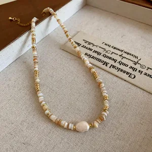 Macro detail of a real gold-plated necklace featuring shell beads and a baroque pearl.