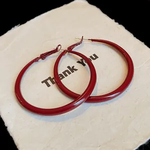 Detail showing dark red enamel hoop earrings presented on a textured white display card
