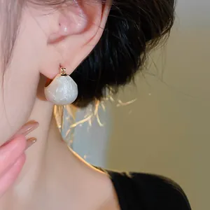 Close-up view of gold-plated retro bean-shaped earrings with a cream marbling texture.