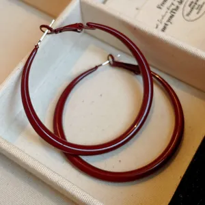 Macro view of large burgundy enamel hoop earrings inside a vintage cream jewelry box