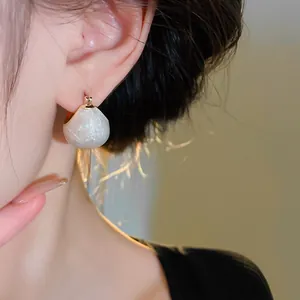 Close-up of minimalist gold-plated teardrop bean earrings with pearly finish
