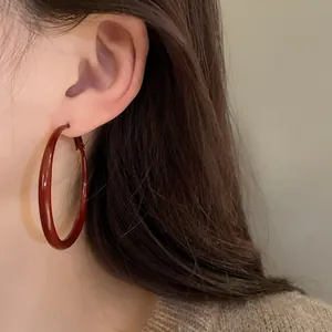 Close-up of a dark red enamel hoop earring worn by a model, showing elegant vintage style