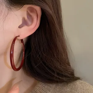 Detailed close-up showing large burgundy drip oil hoop earrings worn by a female model