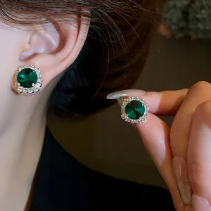 Close-up of elegant emerald green stud earrings featuring a sparkling diamond halo.