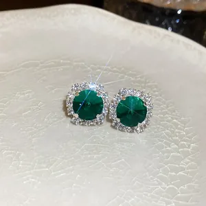 Macro detail of emerald green round earrings with halo diamond setting