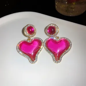 Gros plan détaillé de boucles d'oreilles cœur rose avec strass et bordure dorée.