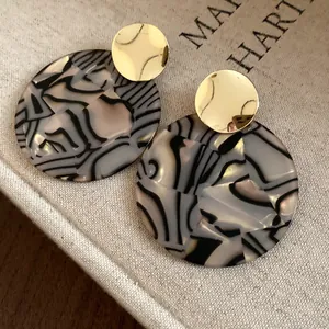 Detailed view of the marbled pattern and polished gold finish of the round earrings.