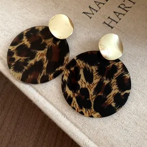 Elegant round leopard print stud earrings with minimalist gold metal details on linen fabric.