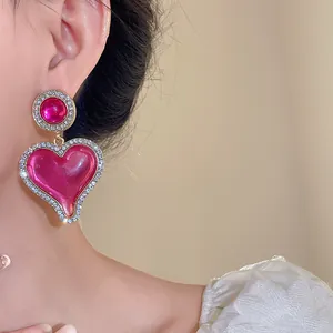 Détail de boucles d'oreilles cœur en résine rose avec bordure de strass brillants.