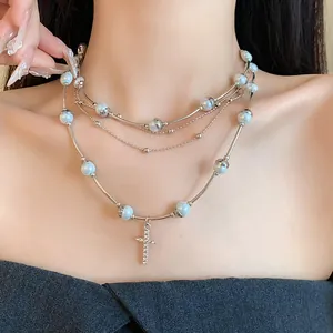 Detail of a multi-layer pearl necklace with a sparkling diamond cross pendant on model.