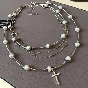 Close-up detail of multi-layered silver necklace with pearls and rhinestone cross pendant.