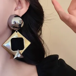Close-up of vintage geometric drop earrings featuring a metallic rhombus and sparkling rhinestone