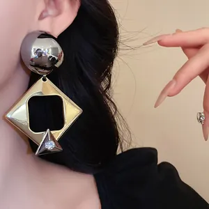 Close-up of exaggerated geometric drop earrings featuring a gold square and silver rhinestone