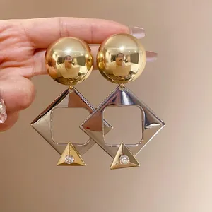 Detailed view of oversized gold and silver geometric diamond earrings with rhinestones