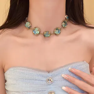 Close-up of vintage court style resin necklace with green stones on a model wearing blue dress.