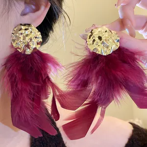 Detailed view of elegant gold crumpled metal earrings with dark red feather tassels.