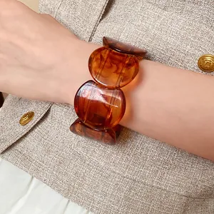 Close-up detail of a stylish amber marbled acrylic round link bracelet worn on a wrist