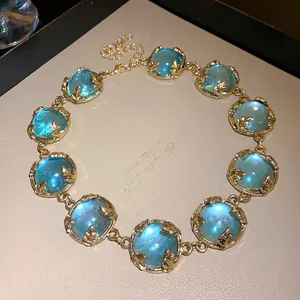 Macro detail of a vintage gold-tone necklace featuring glowing blue resin cabochon stones