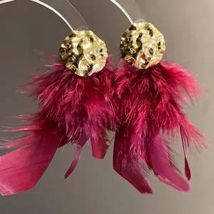 Close-up detail of luxury burgundy feather tassel earrings with gold crumpled metal studs.