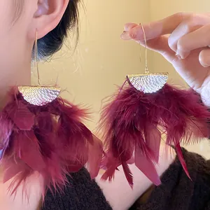 Detail view of dramatic wine red feather tassel earrings with gold crescent top