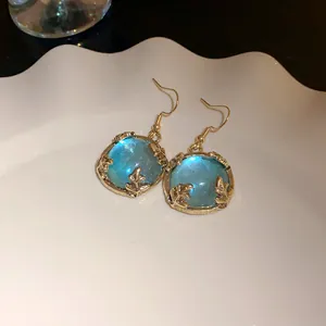 Close-up of vintage palace style gold-toned hook earrings with blue resin stones