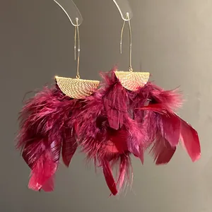 Detailed view of wine red feather tassel earrings with gold textured semi-circle accents.