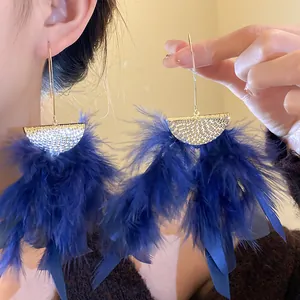 Close-up detail of oversized blue feather tassel earrings with gold textured top.
