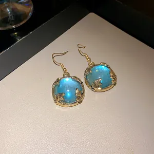 Close-up of vintage gold-tone hook earrings featuring a glowing blue resin centerpiece.