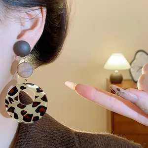 Close-up detail of vintage leopard print wooden dangle earrings worn on a female earlobe.