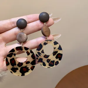 Macro view of leopard print dangle earrings featuring smooth wooden circular studs and gold links