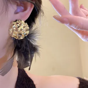 Elegant close-up view of golden crinkled metal disc earrings with dark feather tassels.