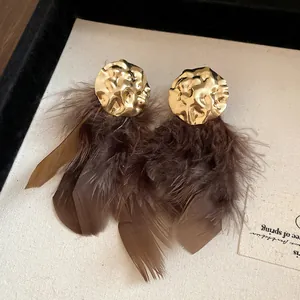 Close-up of vintage gold hammered earrings with fluffy brown feather tassels