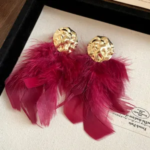 Detail of oversized burgundy red feather tassel earrings with hammered gold-tone metal top