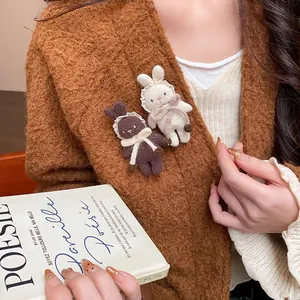 Detailed shot of cute plush rabbit brooches in brown and cream colors on a knitted cardigan