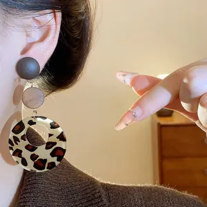 Detailed macro view of retro leopard print tiered earrings with wooden accents worn by a model