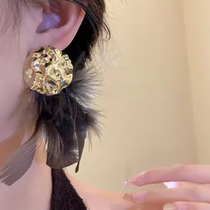 Detail shot of gold crumpled metal stud earring with black feather tassels on ear