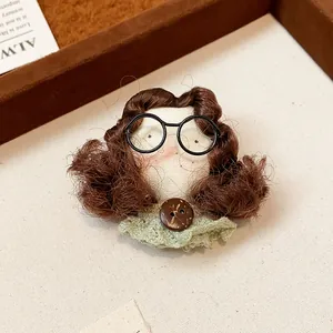 Close-up of handmade doll face brooch with curly brown hair and black glasses