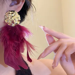 Close-up detail of luxurious burgundy feather tassel earrings with gold wrinkled metal base