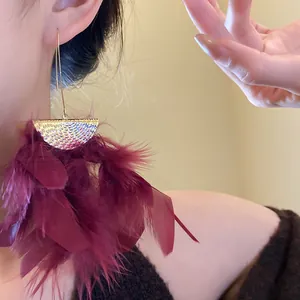 Detailed view of elegant burgundy feather fringe earrings with textured gold top on model