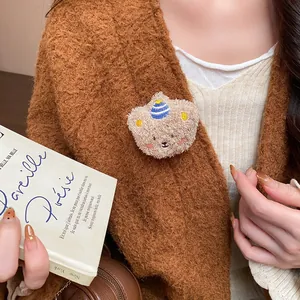 Close-up detail of a cute flocked bear brooch pinned to a brown knitted cardigan.