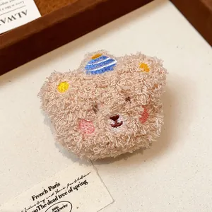 Close-up of a cute plush bear brooch with embroidered features and striped hat.