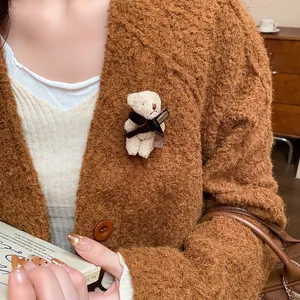Close-up of a cute beige flocked bear brooch with a bow pinned on a brown knit cardigan