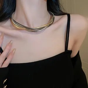 Detailed macro shot of intertwined gold and silver snake chain necklace on model neck area.