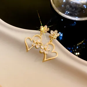 Close-up of gold flower heart drop earrings with shimmering crystals and elegant design.