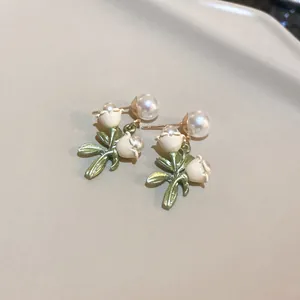 Close-up of elegant pearl flower earrings with green leaf details and silver pins.