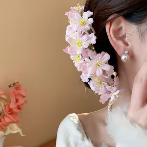 Nahaufnahme einer eleganten rosa Stoffblumen-Haarnadel und Perlenohrringen am Modell.